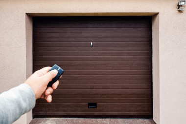 Hand using a remote control to open a brown sectional garage door