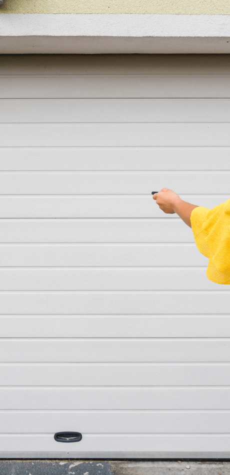 Person in a yellow shirt using a remote control to open a white roller-style garage door.