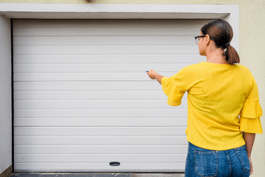 Woman in a yellow top pointing a remote control at a white roller garage door